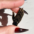 Hand holding a black and gold pin with a palm design against a white background