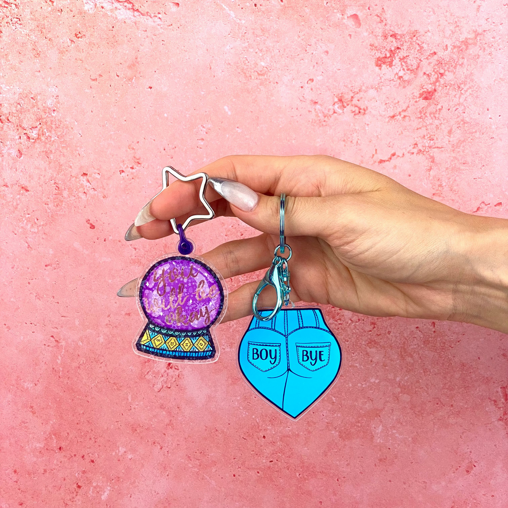 Hand holding two keychains against a pink background