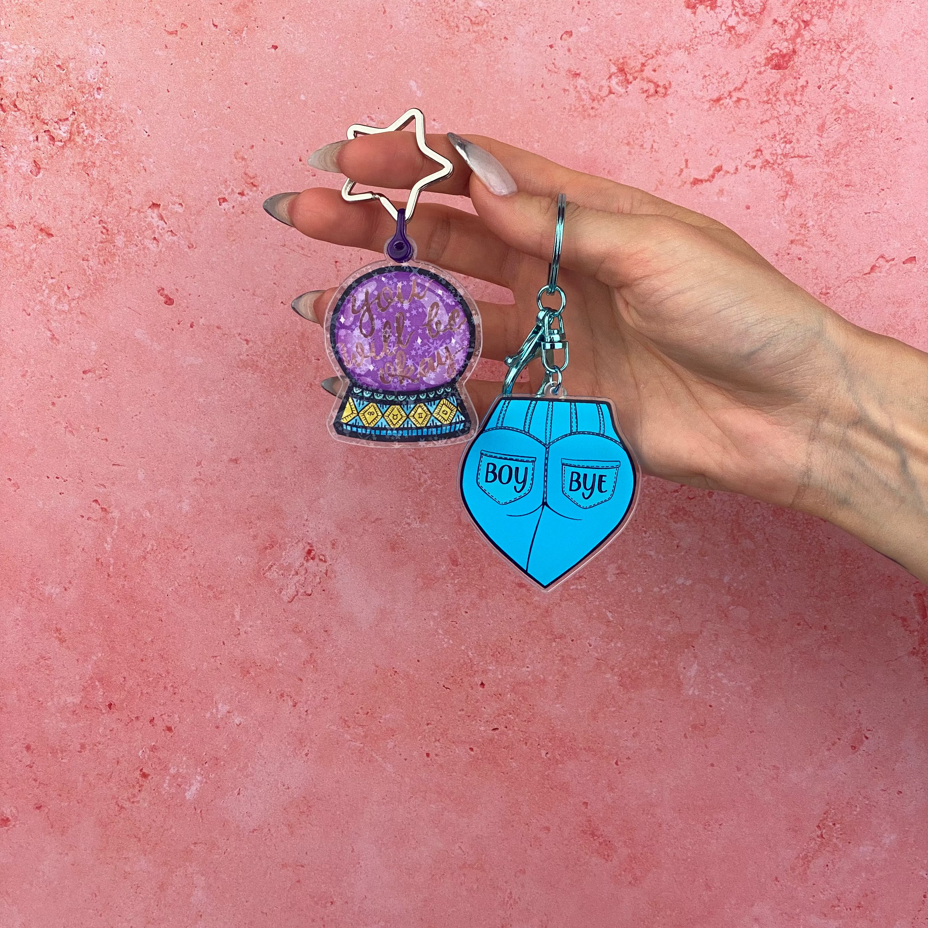 Hand holding two keychains against a pink background