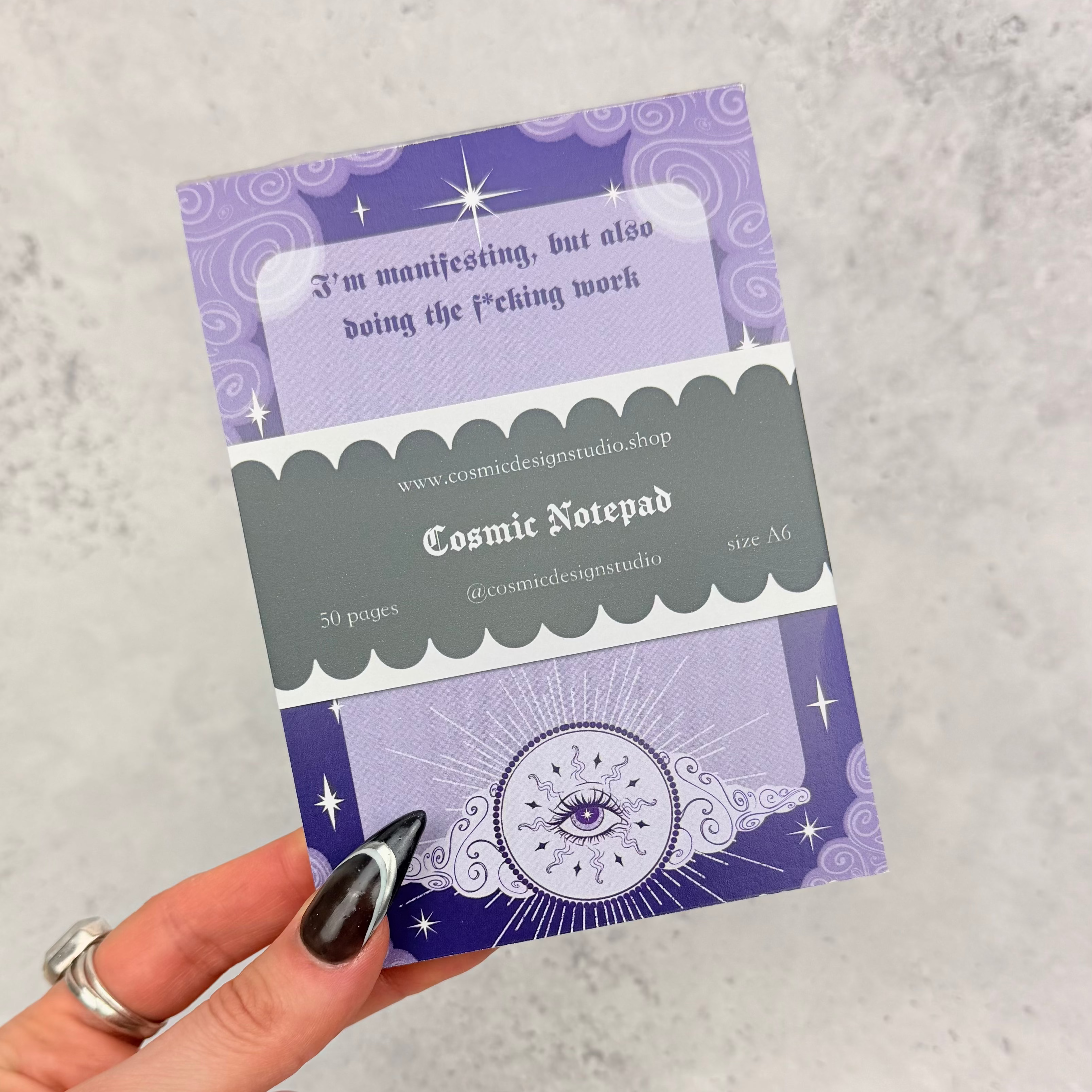 Hand holding a purple and gray Cosmic Notepad against a light gray background