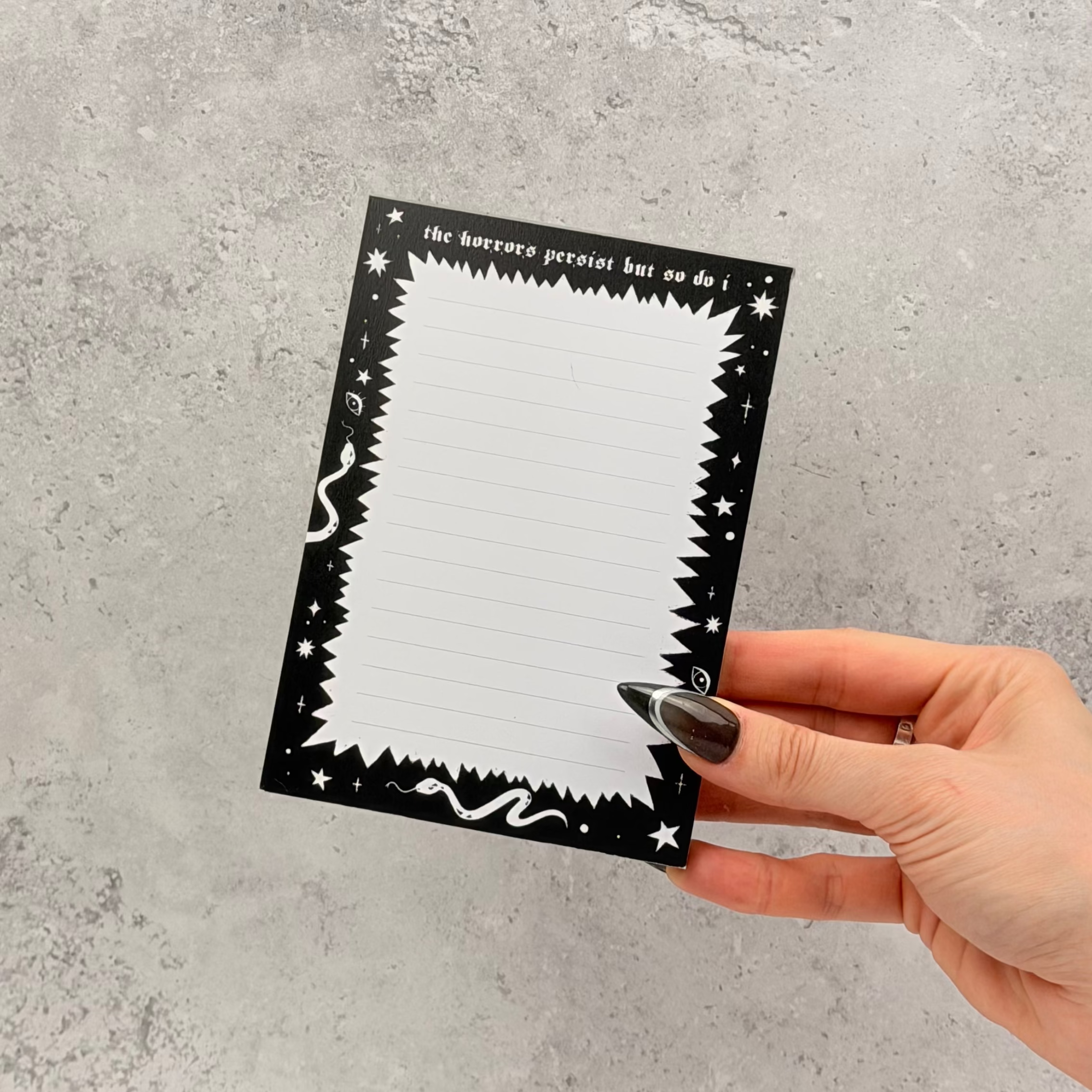 Hand holding a black and white notepad against a gray textured background