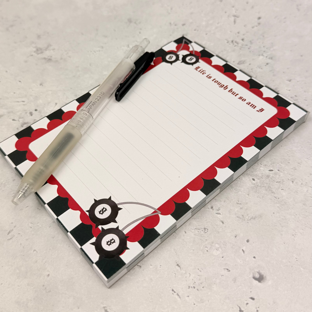 Notepad with a red and black checkered border and a pen on a gray surface