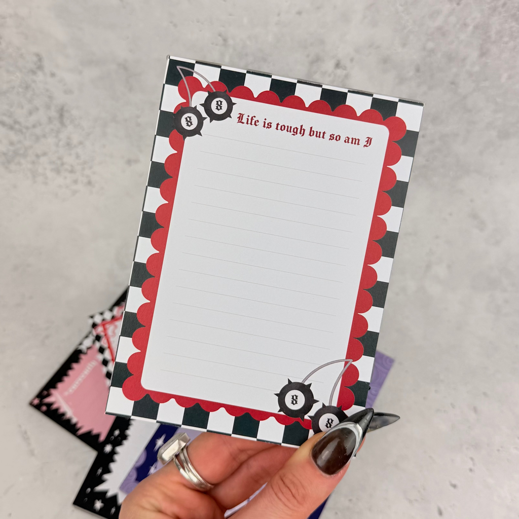 Hand holding a decorative notepad with checkered border and text on a gray surface