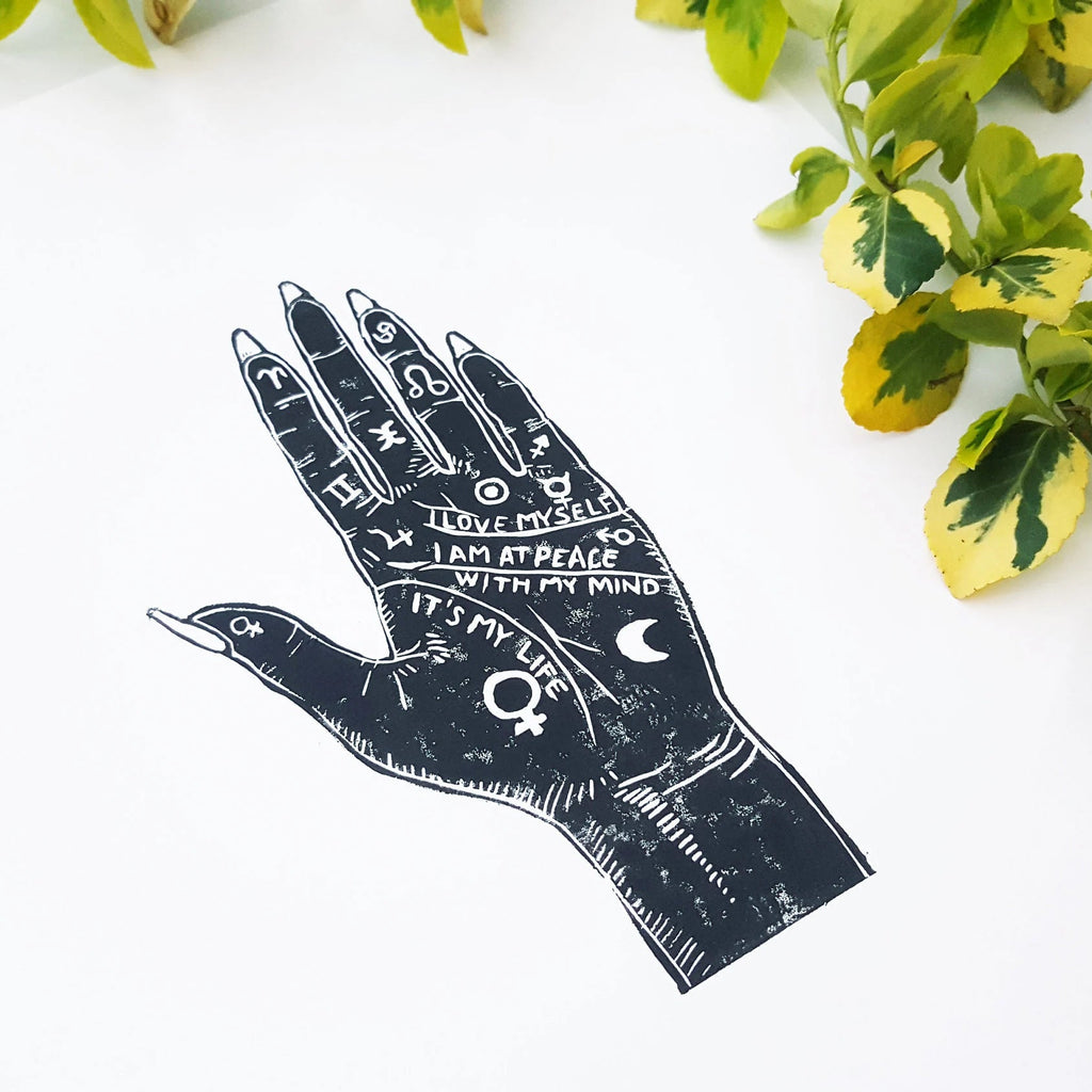 Black and white illustration of a palmistry hand with symbols on a white background with green leaves.