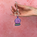Hand holding a purple crystal ball keychain with star design against a pink background